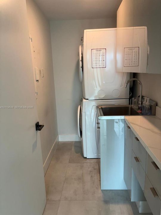 Laundry area featuring a stacked laundry unit, built-in cabinetry with stone-finish countertops, stainless steel basin, and gooseneck faucet