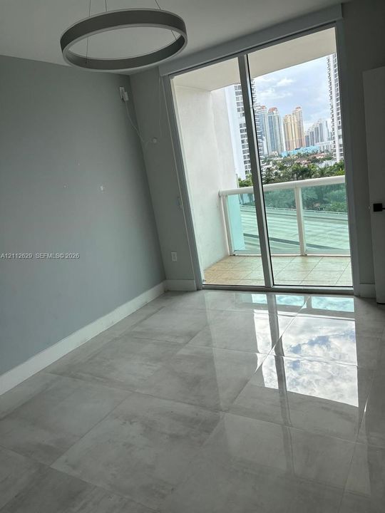 Floor-to-ceiling sliding glass doors, large-format tile flooring, private balcony with glass railing, and a contemporary circular pendant light fixture