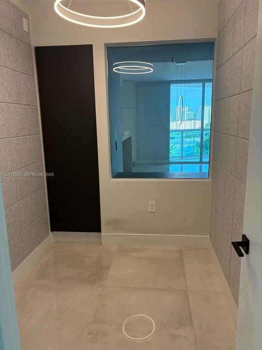 Interior space featuring large-format tile flooring, textured wall paneling, a rectangular built-in niche with an expansive interior window, and a modern circular LED light fixture