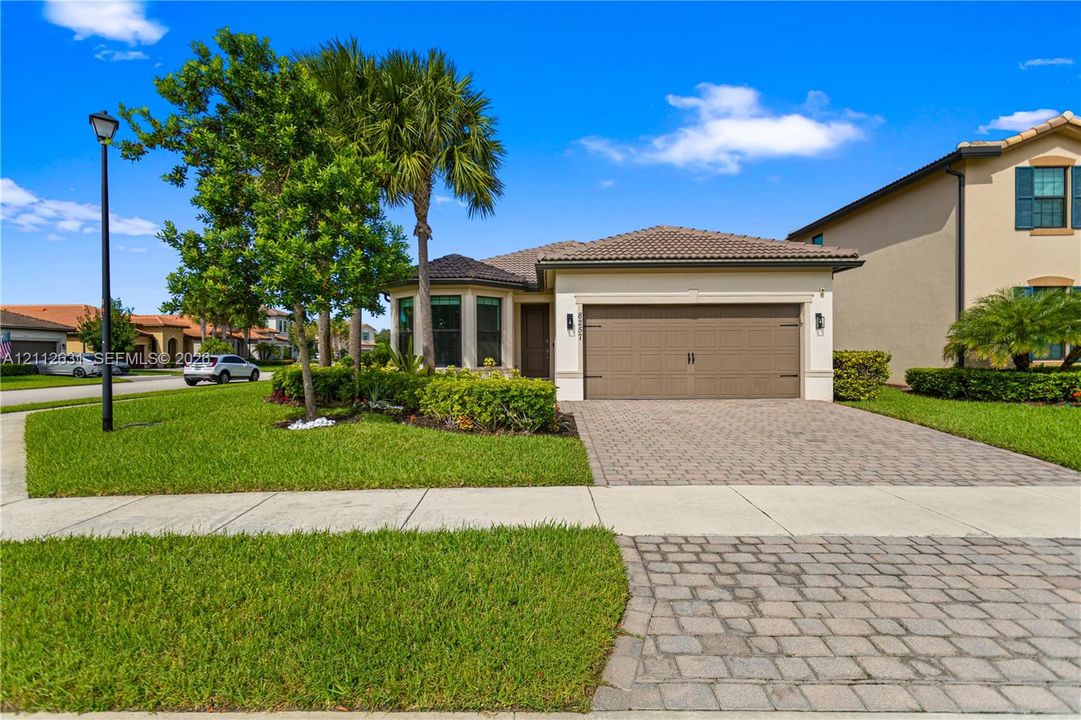 Stucco exterior with a tiled roof, paver driveway, and an attached two-car garage