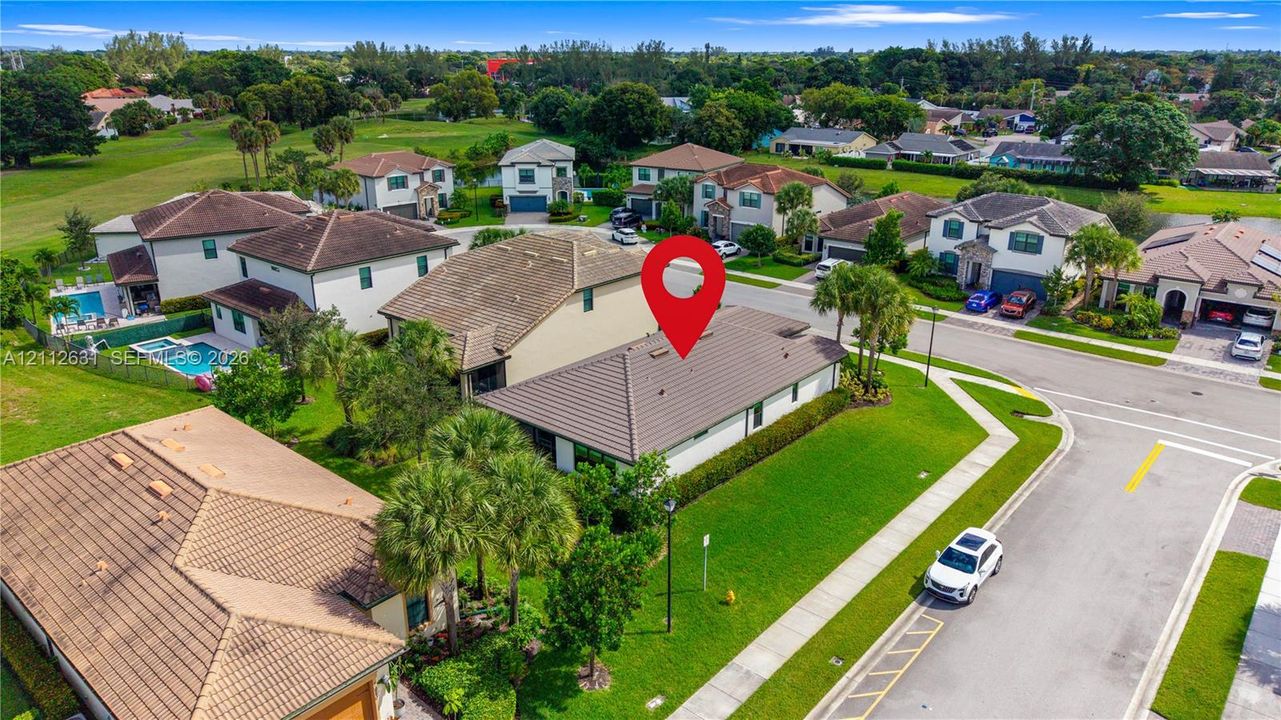 Aerial perspective of a corner lot property featuring a tiled roof, manicured lawn, and mature palm landscaping