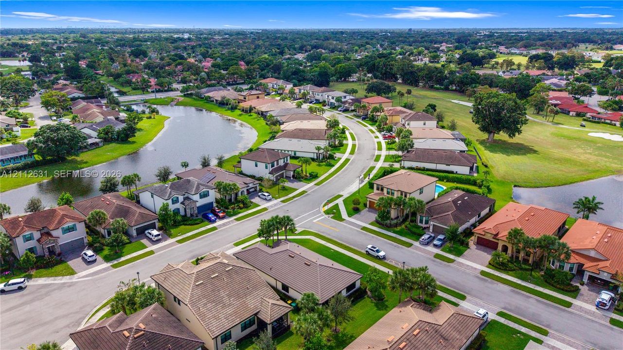 Aerial perspective of residential neighborhood featuring a winding lake, paved streets, manicured green space, and tile-roofed homes