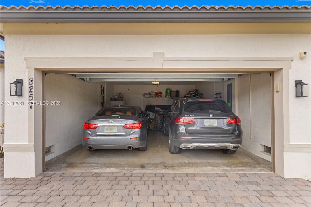Two-car garage featuring a concrete floor, stucco exterior finish, tile roof, and wall-mounted exterior lanterns