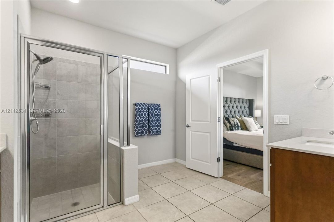 Walk-in shower with floor-to-ceiling ceramic tile surround and chrome fixtures, wood-finish vanity with countertop sink, and neutral ceramic tile flooring
