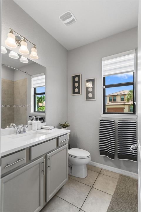 Bathroom featuring a white countertop vanity with gray cabinetry, a wall-to-wall mirror, a three-light fixture, and ceramic tile flooring