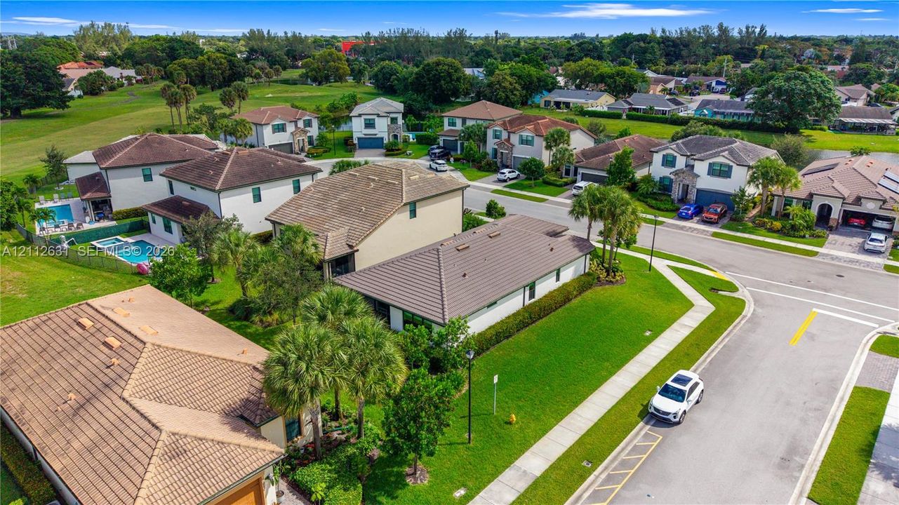 Aerial perspective of a residential neighborhood featuring multi-story dwellings, tile roofing, manicured green spaces, and palm tree landscaping