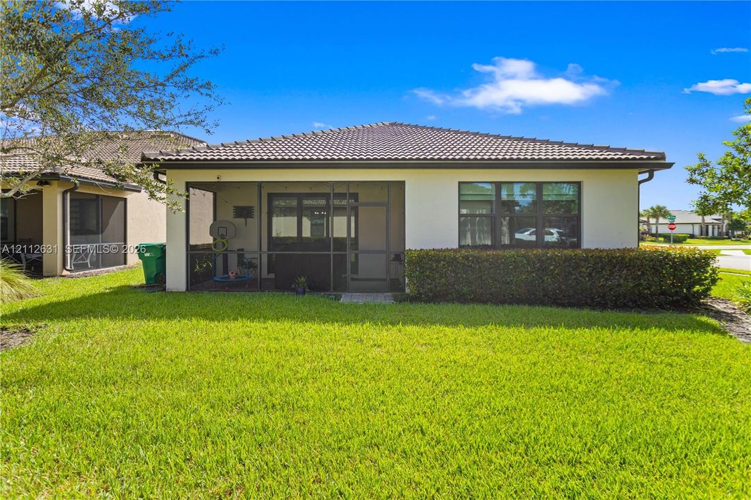 Exterior rear elevation featuring a screened-in lanai, stucco facade, tiled roof, and manicured lawn