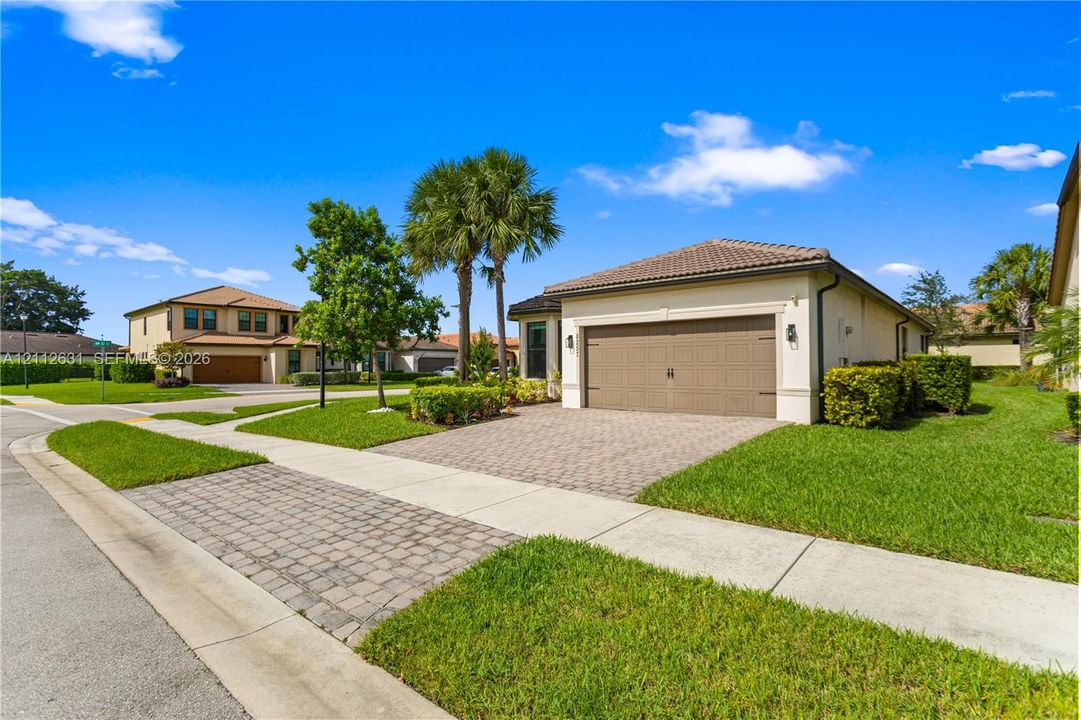 Stucco exterior featuring a paver driveway, multi-car garage, and mature landscaping