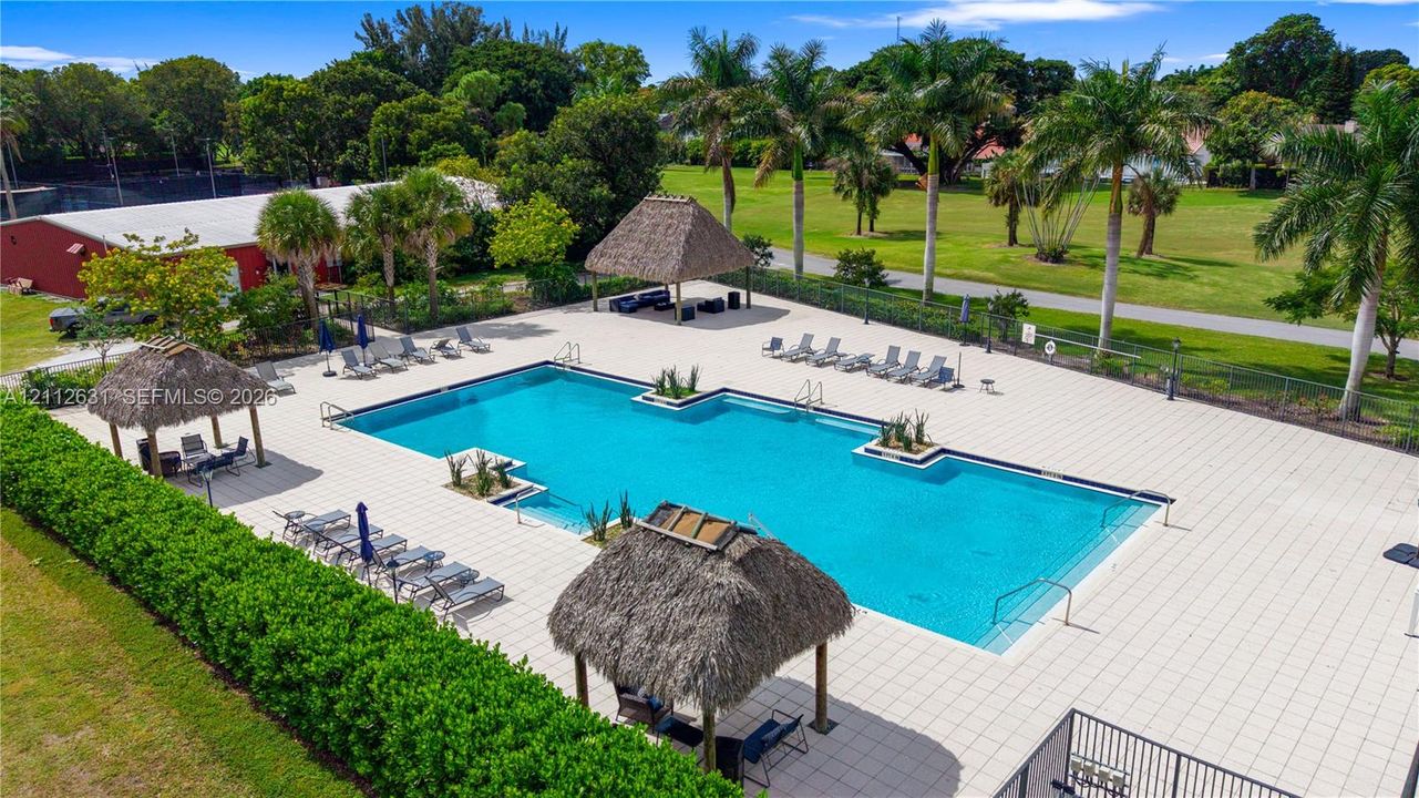 In-ground swimming pool featuring a large concrete deck, integrated planters, and multiple thatched-roof cabanas