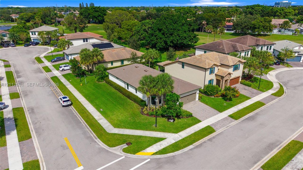 Corner lot residence featuring a paved driveway, tile roofing, manicured lawn, and perimeter landscaping
