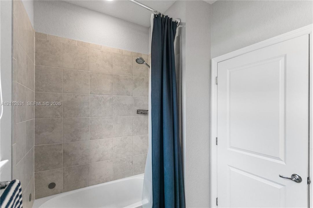 Bathtub with a shower head, tiled surround, built-in shelving niche, and a panel door with brushed metal hardware