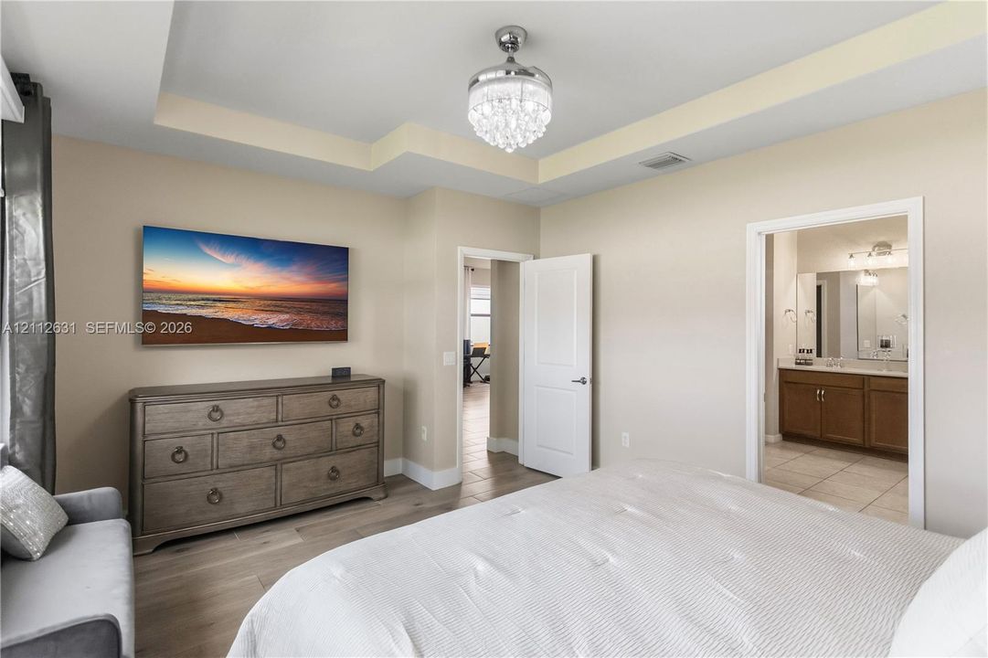 Tray ceiling, crystal-style ceiling fan fixture, wood-finish flooring, and solid-core interior door