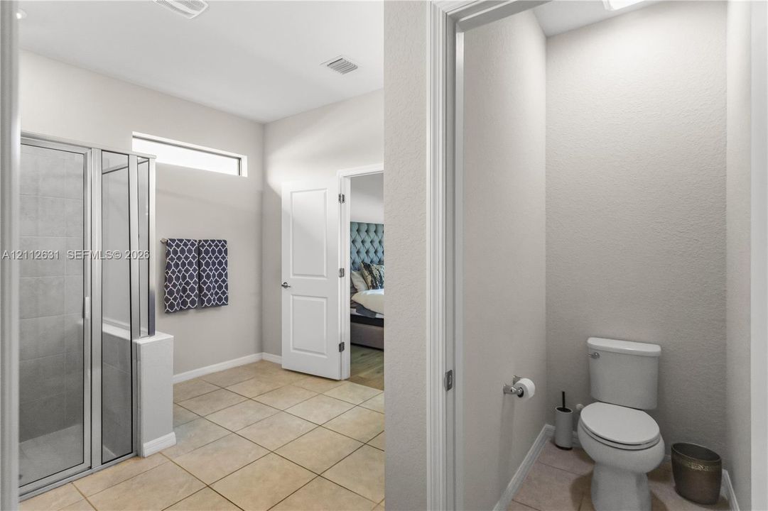 Shower enclosure with framed glass door, tile flooring, high-set horizontal window, and enclosed water closet