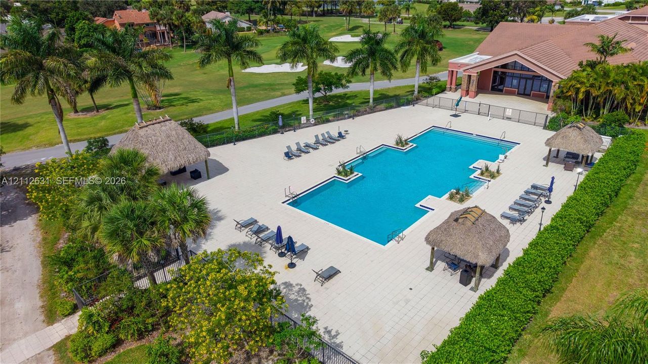 Rectangular swimming pool featuring a tiled deck, multiple thatched-roof structures, and perimeter landscaping