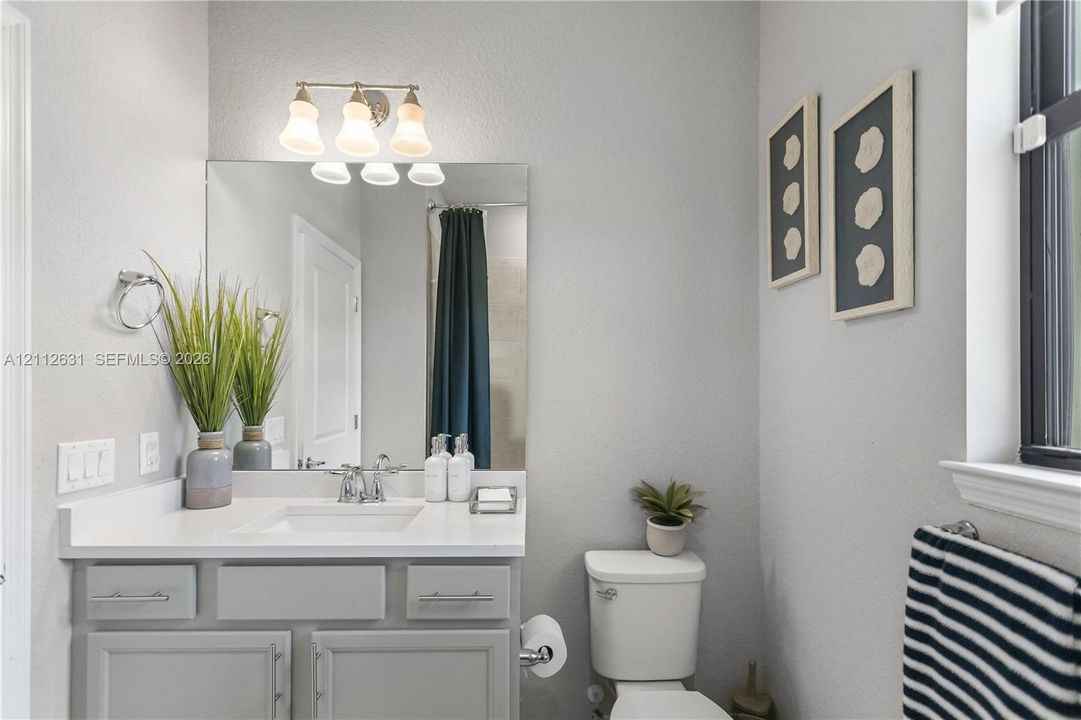 Bathroom featuring a light-toned vanity with a rectangular undermount sink, solid surface countertop, polished chrome fixtures, and a triple-light wall-mounted fixture above a rectangular mirror