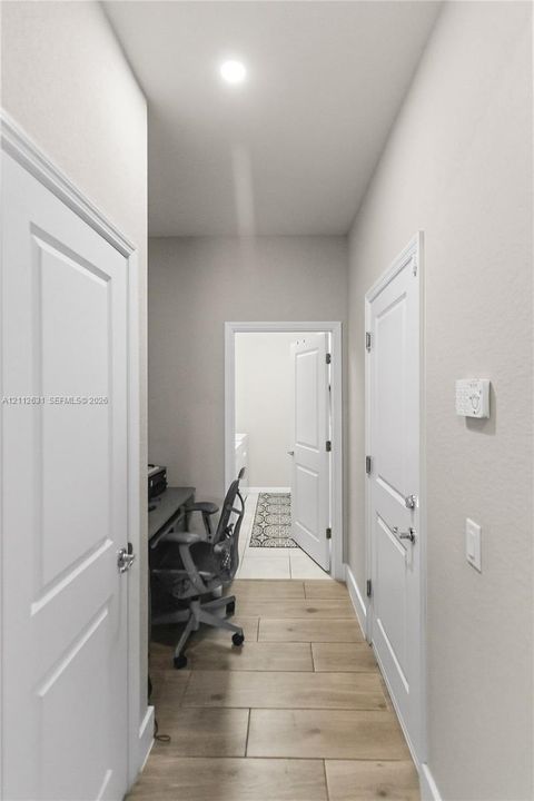Hallway featuring wood-finish tile flooring, recessed ceiling lighting, and multiple two-panel interior doors
