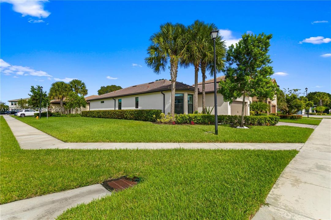 Corner lot featuring a stucco exterior, a tiled roof, mature palm trees, and manicured hedges