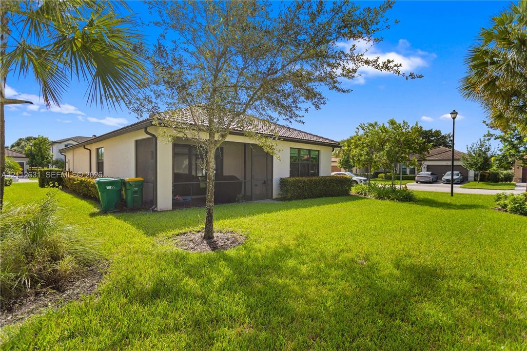 Stucco exterior featuring a tiled roof, screened-in porch, mature landscaping, and an expansive lawn