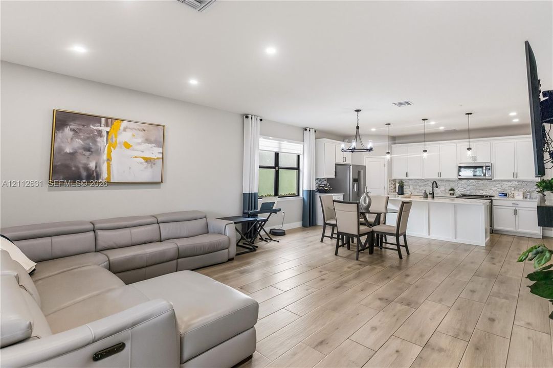 Open-concept living space featuring wood-finish flooring, recessed lighting, white shaker-style cabinetry, a kitchen island, and a decorative chandelier