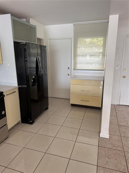 Kitchen featuring ceramic tile flooring, glossy flat-panel cabinetry, a built-in black refrigerator, and a solid-surface countertop
