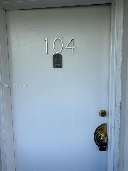 Solid door entry featuring metallic house numbering, a peephole, and a brass-tone lever handle set