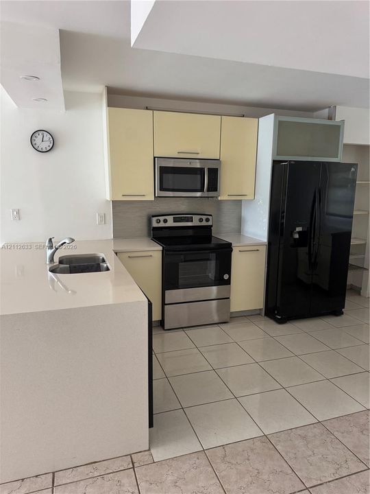 Kitchen featuring pale cabinetry, a stainless steel electric range, a microwave, a large-format refrigerator, and a solid-surface peninsula with an integrated sink