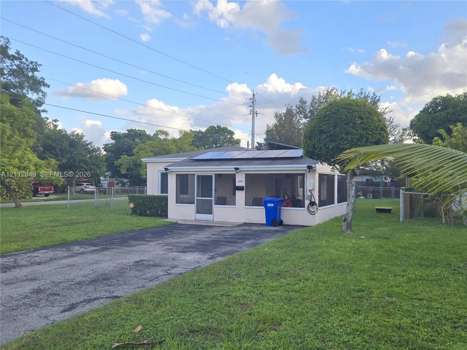 Single-story exterior featuring a screened-in porch, roof-mounted solar panels, asphalt driveway, and expansive lawn