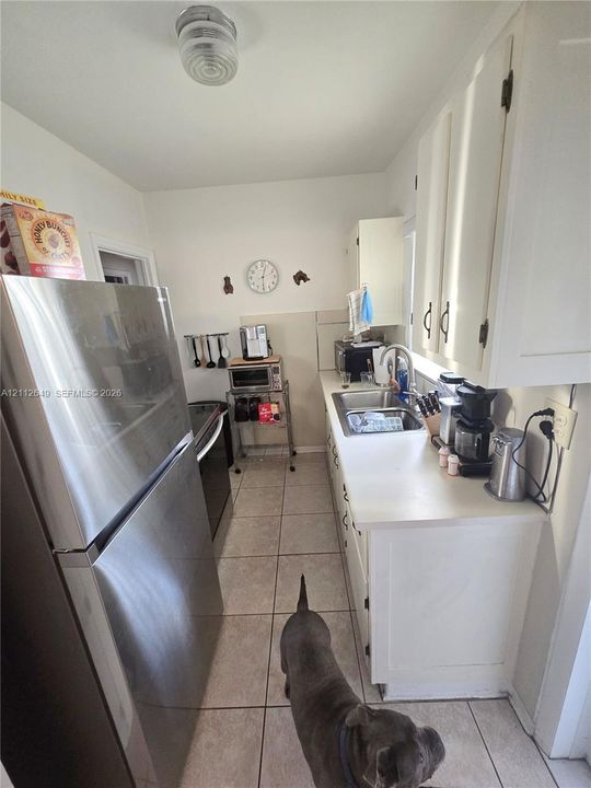 Kitchen featuring white cabinetry, stainless steel refrigerator, stainless steel sink with a high-arch faucet, and tile flooring