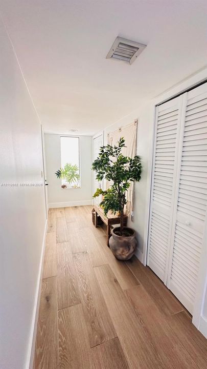 Hallway featuring wood-finish flooring, white louvered closet doors, and an elongated rectangular window