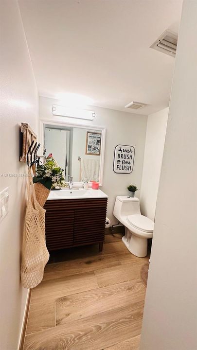 Bathroom featuring a ribbed wood-finish vanity, integrated sink basin, white-framed wall mirror, wall-mounted light fixture, and wood-finish flooring