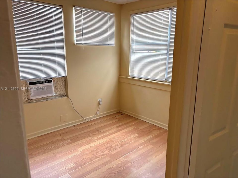 Room interior featuring wood-finish flooring, three windows with horizontal blinds, and a built-in wall-mounted air conditioning unit