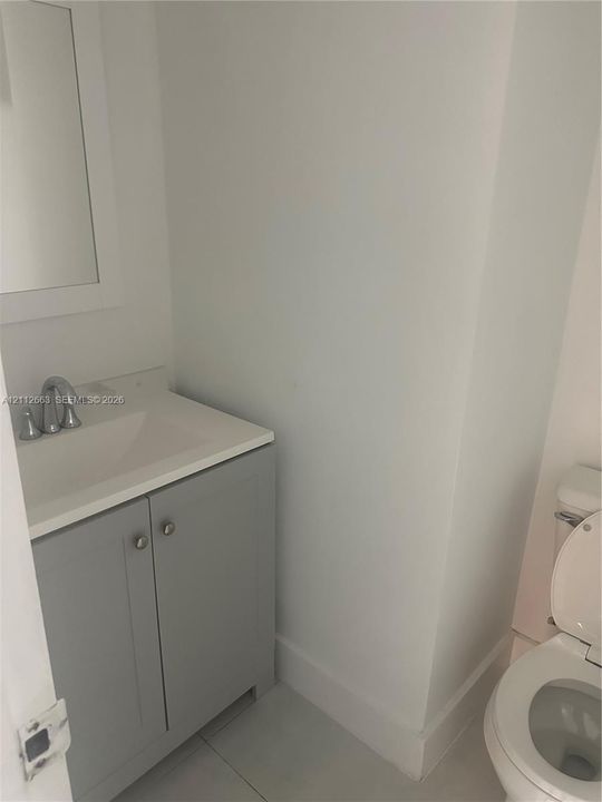 Grey shaker-style vanity with a solid-surface integrated countertop, brushed metal faucet, and wall-mounted mirror