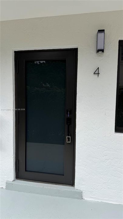 Entryway featuring a dark-toned door with glass paneling, stucco exterior wall, and wall-mounted exterior light fixture
