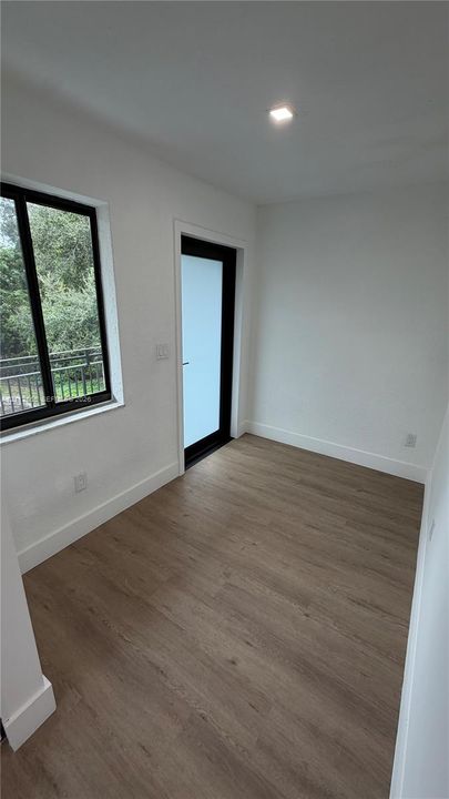 Neutral-toned wood-finish flooring, single-hung window with black framing, glass-paneled door with black frame, and recessed ceiling lighting