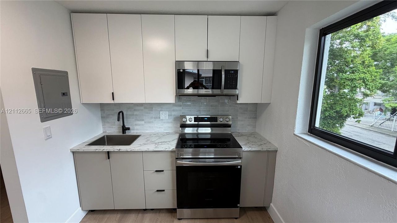 Kitchenette featuring white upper cabinetry, grey lower cabinetry, stone-patterned countertops, stainless steel appliances, and a matte black faucet