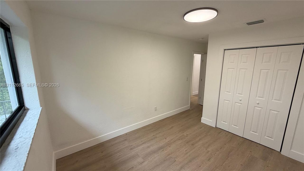 Interior space featuring wood-finish flooring, a large window with a deep sill, neutral wall finishes, a flush-mount circular lighting fixture, and a white bi-fold closet door