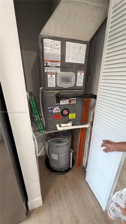 Mechanical closet housing a gas furnace unit and electric water heater, enclosed by louvered doors