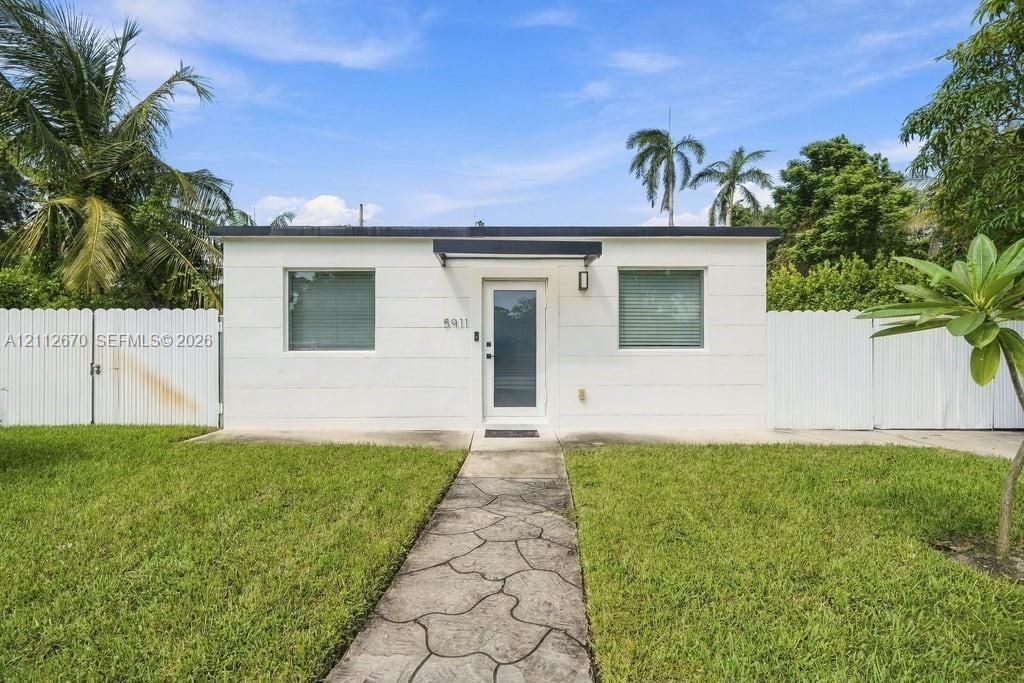 Exterior facade featuring crisp white stucco siding, a flat roofline, a glass-panel entry door, and a decorative concrete walkway surrounded by privacy fencing
