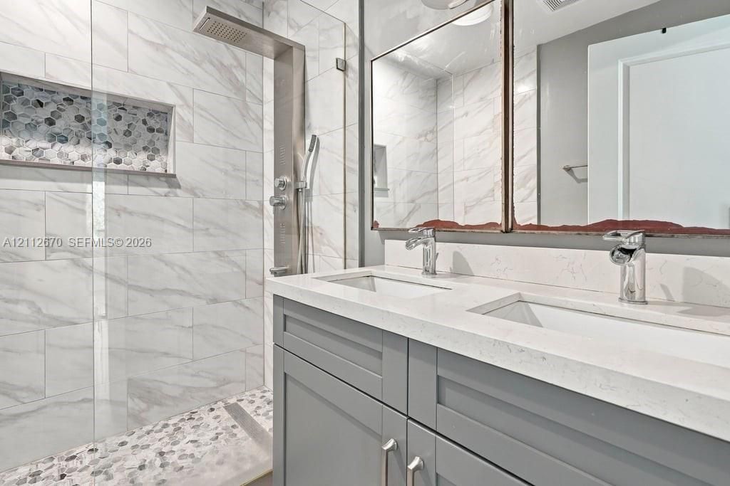 Double vanity with quartz countertop, walk-in shower with stone-tile flooring, inset wall niche, rainfall showerhead, and dual polished-chrome faucets