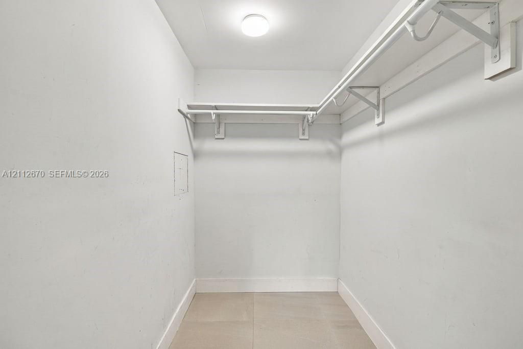 Storage area featuring white walls, large-format tile flooring, and custom-installed overhead shelving with hanging rods