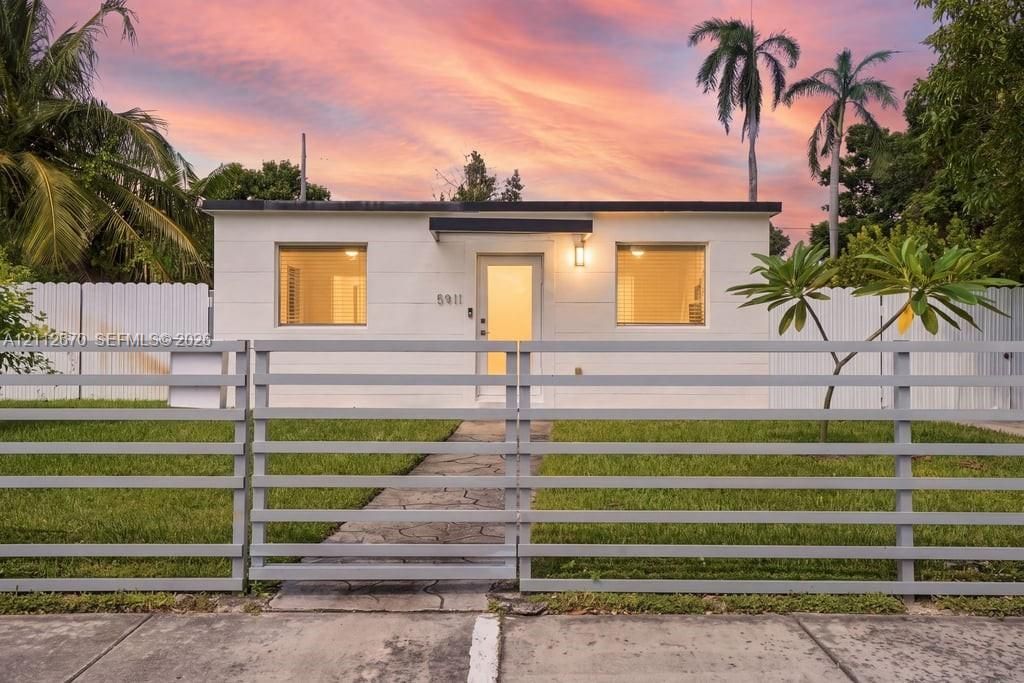 Single-story exterior featuring a horizontal slat perimeter fence, stone-paved walkway, manicured lawn, and wall-mounted exterior lighting