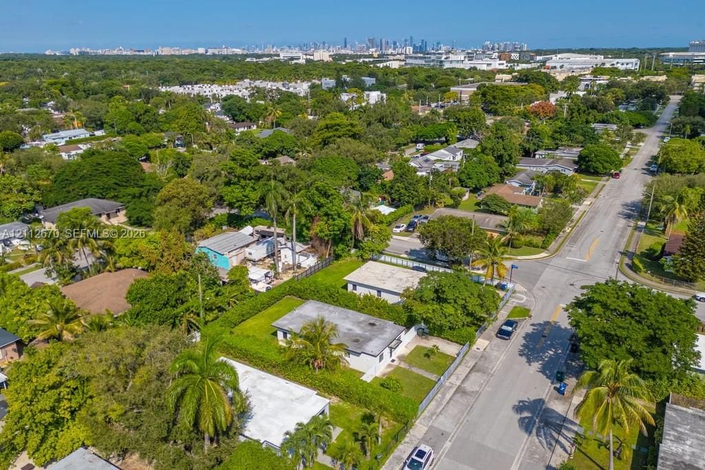Aerial perspective featuring a flat-roof residence, expansive green space, mature tropical landscaping, and a distant city skyline