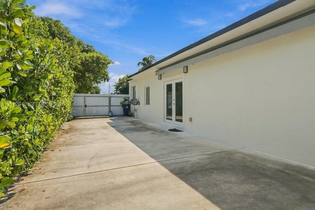 Concrete paved exterior area featuring white stucco siding, dual glass-panel entry doors, and a solid perimeter privacy gate