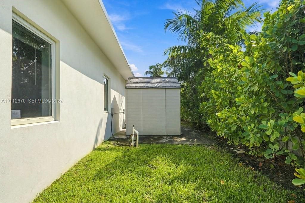 Stucco exterior with sliding windows, standalone storage shed, and manicured landscaping