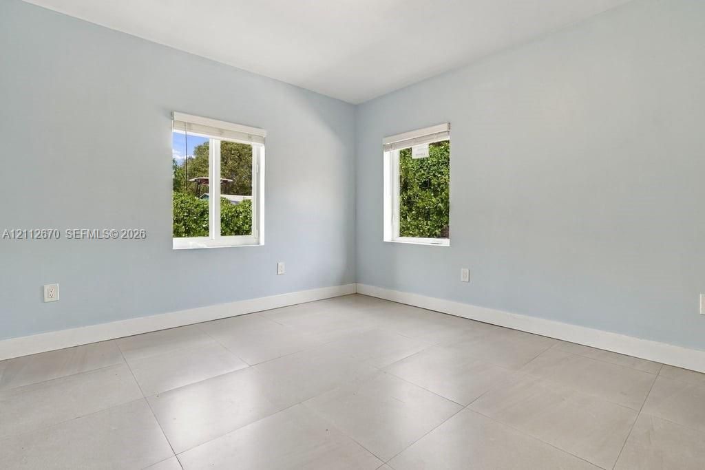 Neutral-toned room featuring large-format tile flooring, light-colored wall paint, and dual windows equipped with roller shades