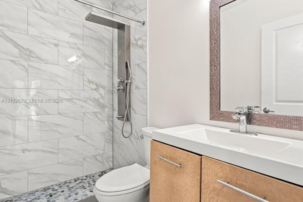 Walk-in shower featuring large-format tile surround, river stone flooring, and a stainless steel shower panel system, paired with a custom wood-finish vanity and integrated rectangular sink