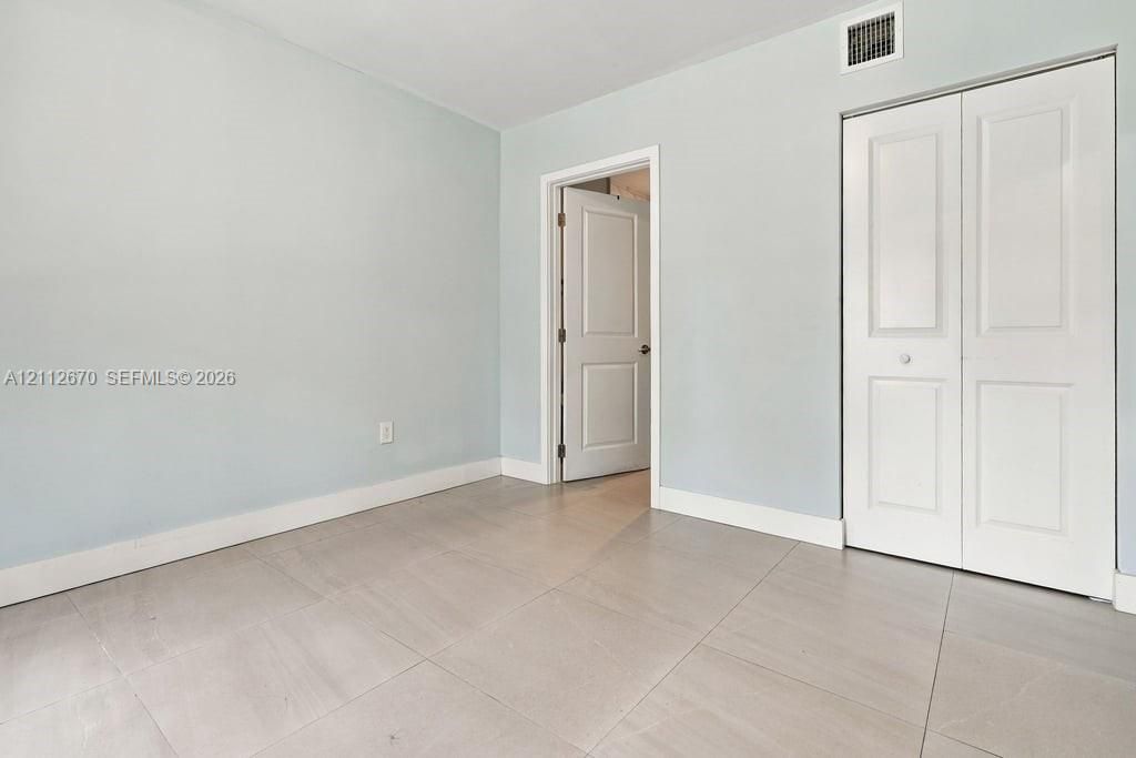 Neutral-toned room featuring large-format tile flooring, a two-panel interior door, and a built-in closet with double-panel doors