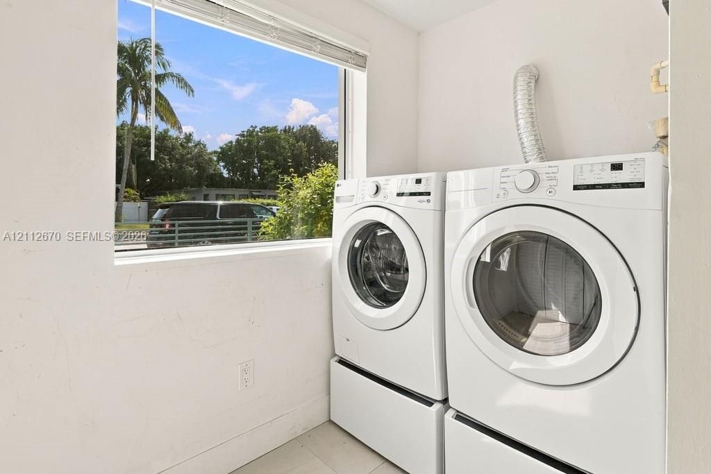 Laundry area featuring white appliances, tile flooring, and a large window