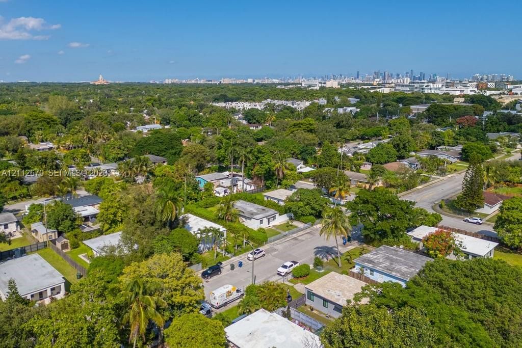 Aerial perspective of a neighborhood setting featuring mature trees, paved streets, and a distant urban skyline