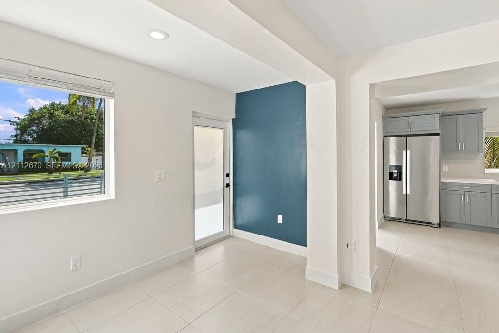 Open-concept floor plan featuring large-format ceramic tile flooring, a blue accent wall, recessed lighting, and a glass-paneled entry door